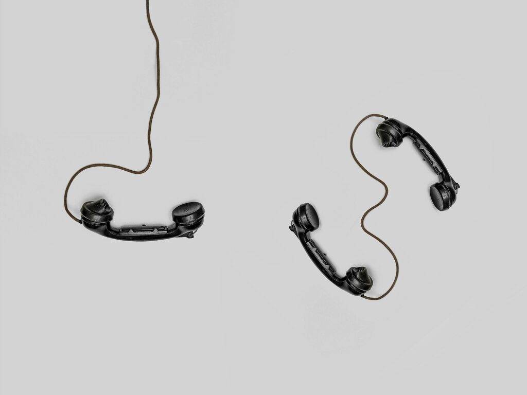 Two vintage black telephone handsets connected by cords on gray background.